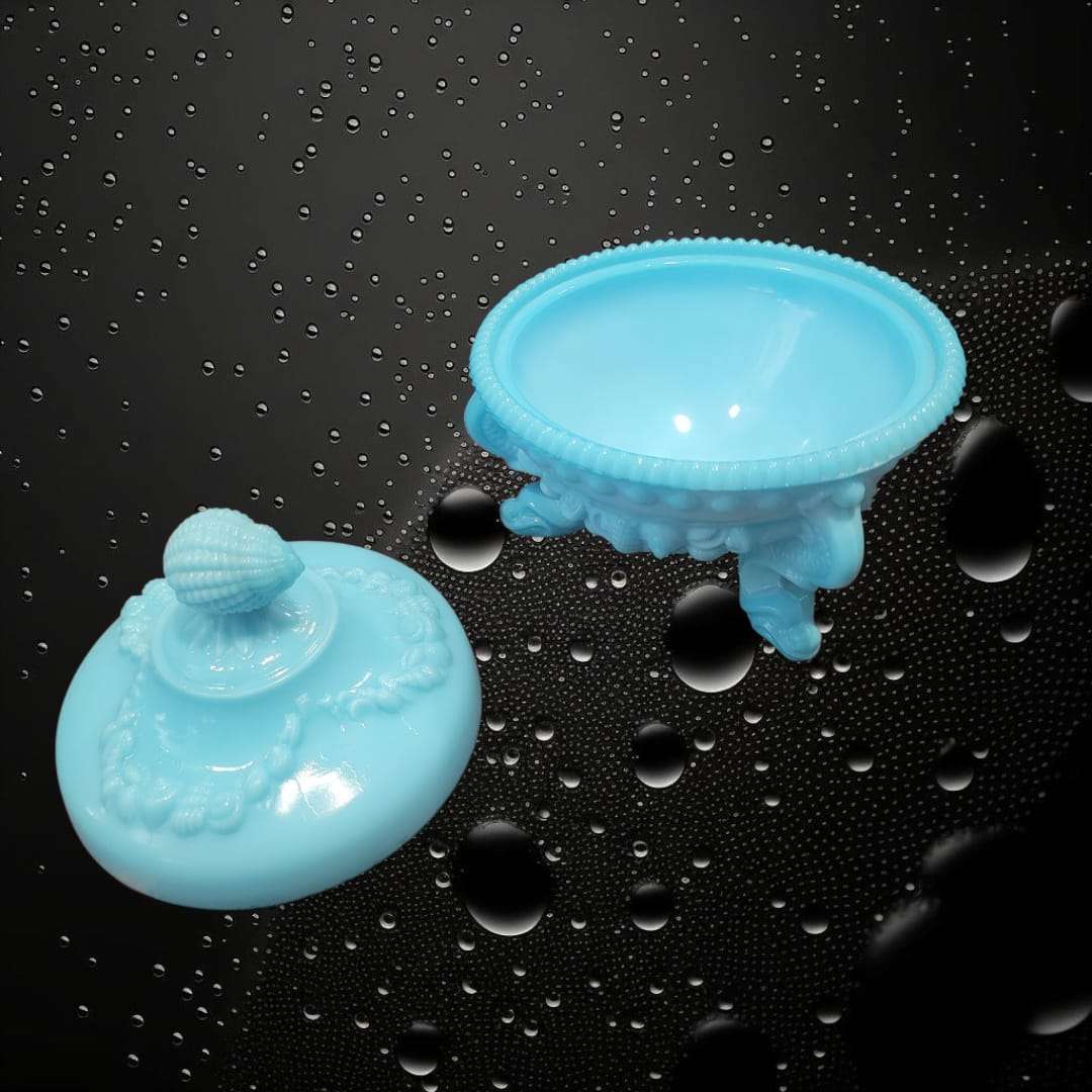 Bombonera de opalina azul abierta, mostrando su interior liso y tapa decorativa con forma de concha. Perfecta para frutero o adorno clásico.