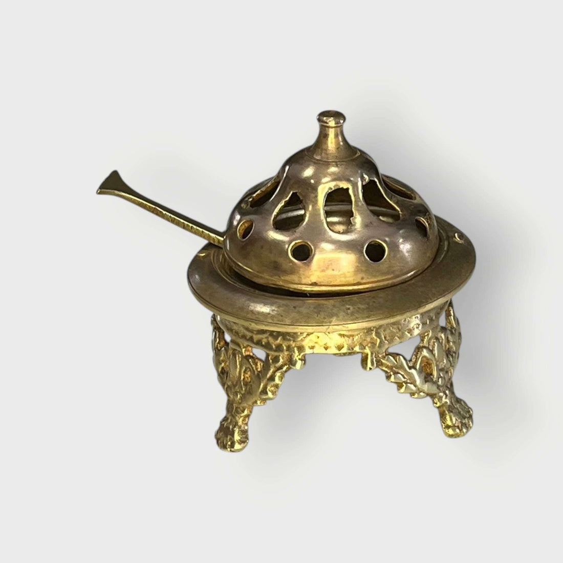 Brasero de metal dorado con badilla en vista frontal sobre fondo neutro.