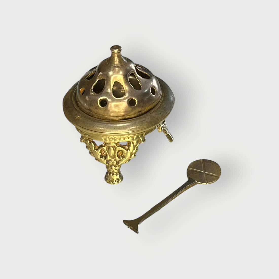 Brasero de metal dorado con badilla en vista frontal sobre fondo neutro.