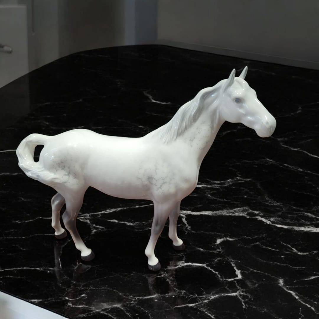 Caballo de porcelana Beswick blanco con detalles realistas, sobre superficie de mármol negro. Elegancia ecuestre clásica para decoración de interiores.