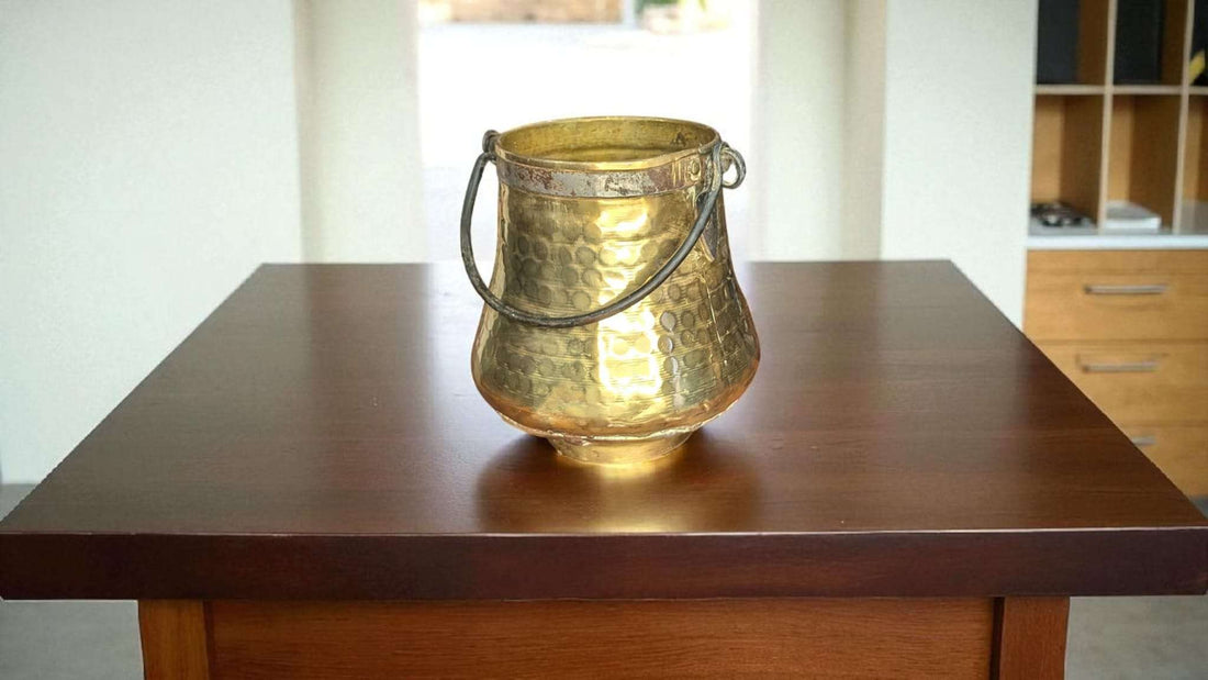 Caldero Antiguo de Metal Dorado con Asa de Forja – Elegancia sobre mesa de madera, ideal para decoración rústica en interiores de hogar.