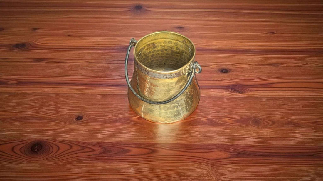 Caldero Antiguo de Metal Dorado con Asa de Forja – Elegancia sobre mesa de madera, ideal para decoración rústica en interiores de hogar.