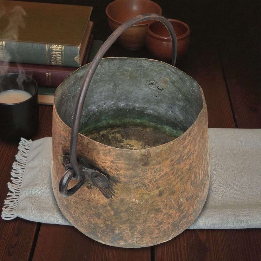 Caldero de cobre con acabado oxidado y asa de hierro.