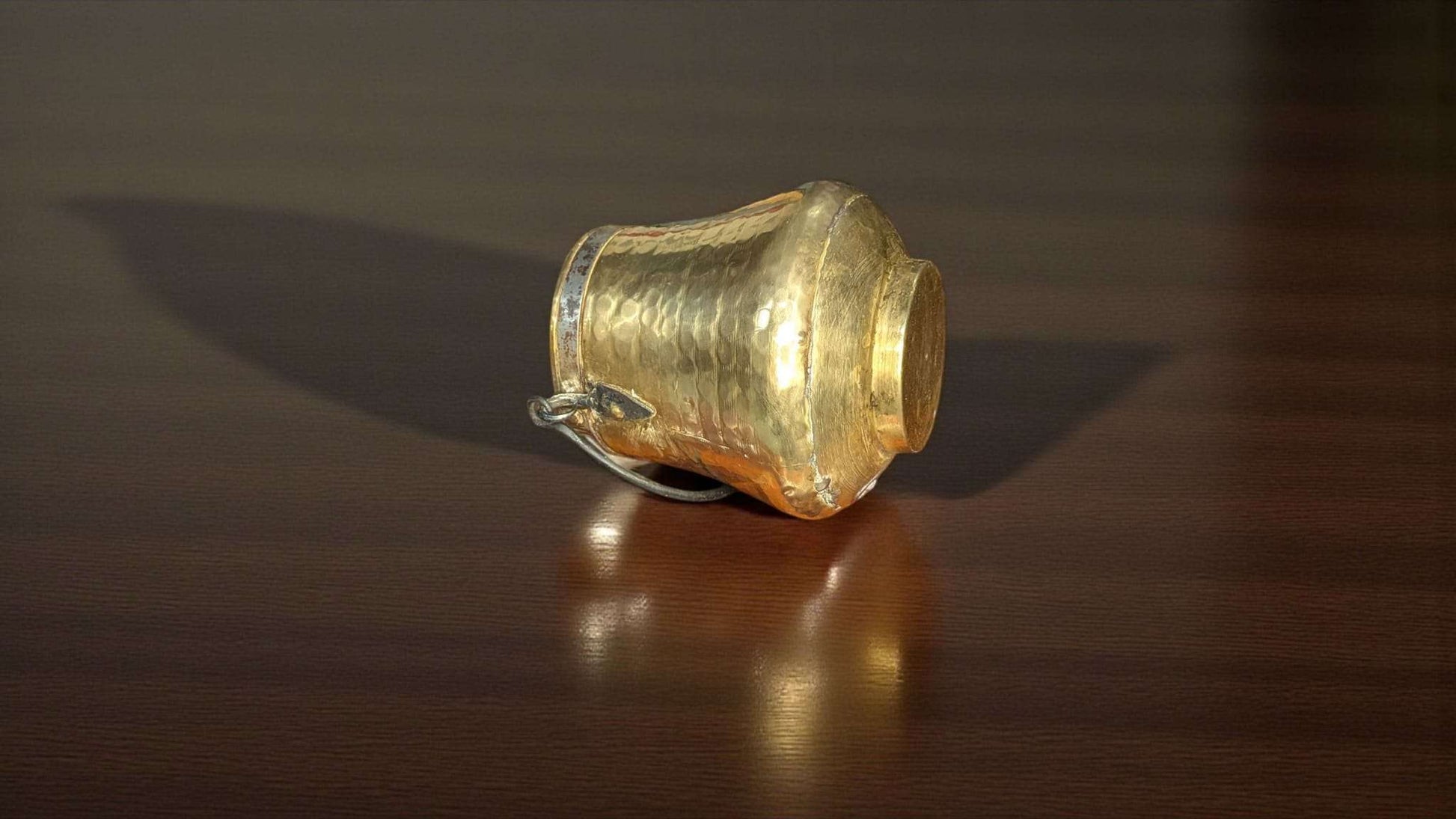 Caldero antiguo de metal dorado con asa de forja sobre superficie de madera, ideal para decoración rústica y elegante en el hogar o jardín.