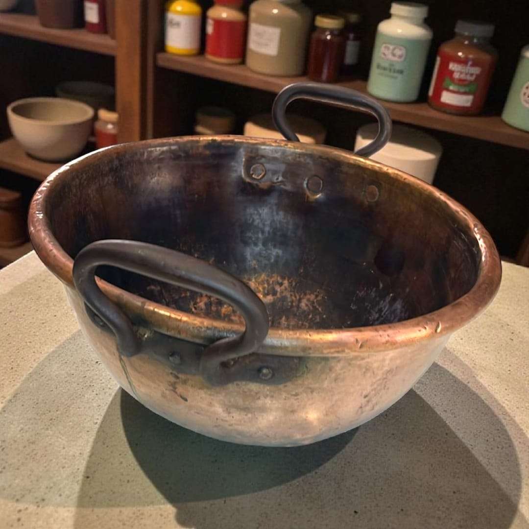 Caldero de cobre con asas de forja artesanal sobre mesa rústica.