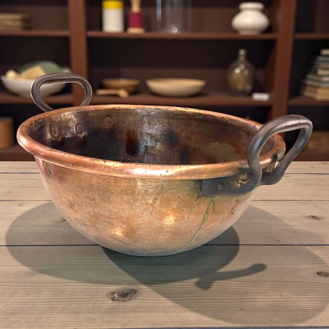 Caldero de cobre con asas de forja artesanal sobre mesa rústica.