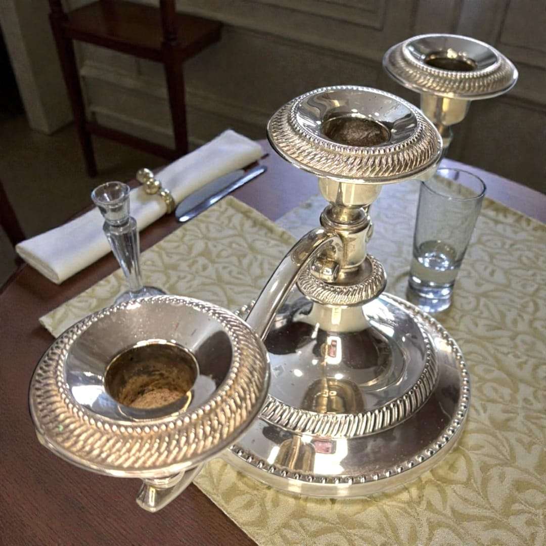 Candelabro de tres velas en metal plateado vintage sobre mesa elegante con vajilla clásica. Ideal para decoración de cenas y eventos formales.