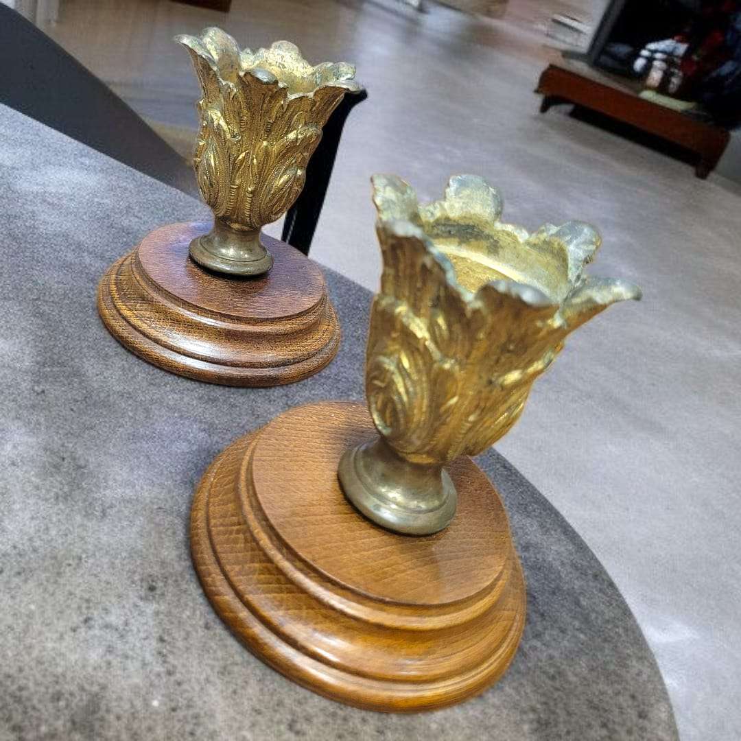 Candeleros de bronce antiguo con base de madera torneada vistos en perspectiva.