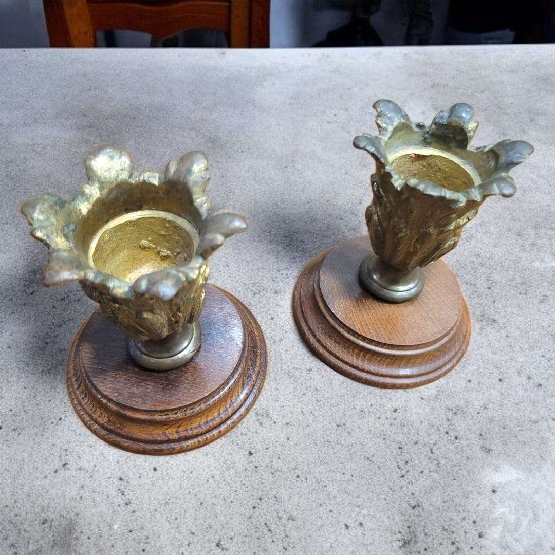 Candeleros de bronce antiguo con base de madera torneada vistos en perspectiva.