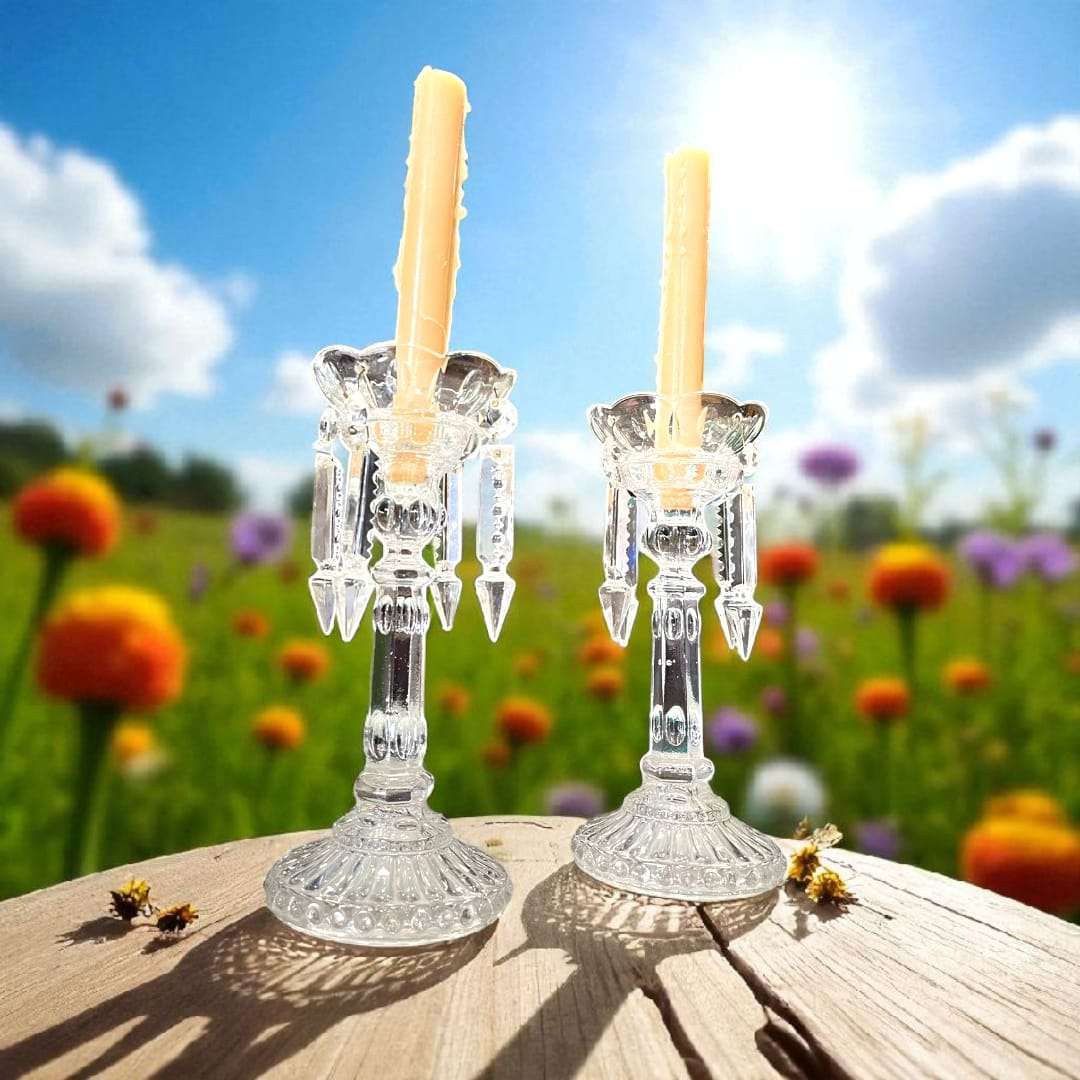 Pareja de candeleros de cristal antiguos sobre mesa con pétalos, ideales para decoración elegante y tradicional en jardín primaveral.