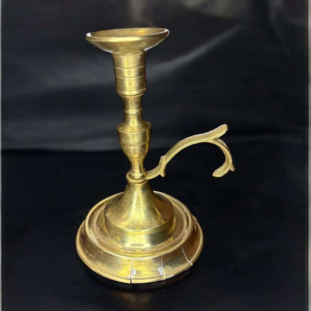 La Palmatoria de metal dorado es un objeto tradicional diseñado para sujetar velas y permitir su transporte seguro gracias a su asa lateral. 