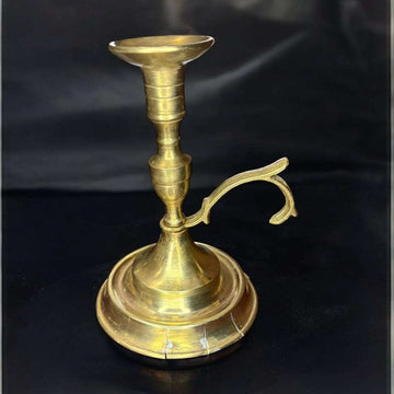 La Palmatoria de metal dorado es un objeto tradicional diseñado para sujetar velas y permitir su transporte seguro gracias a su asa lateral. 