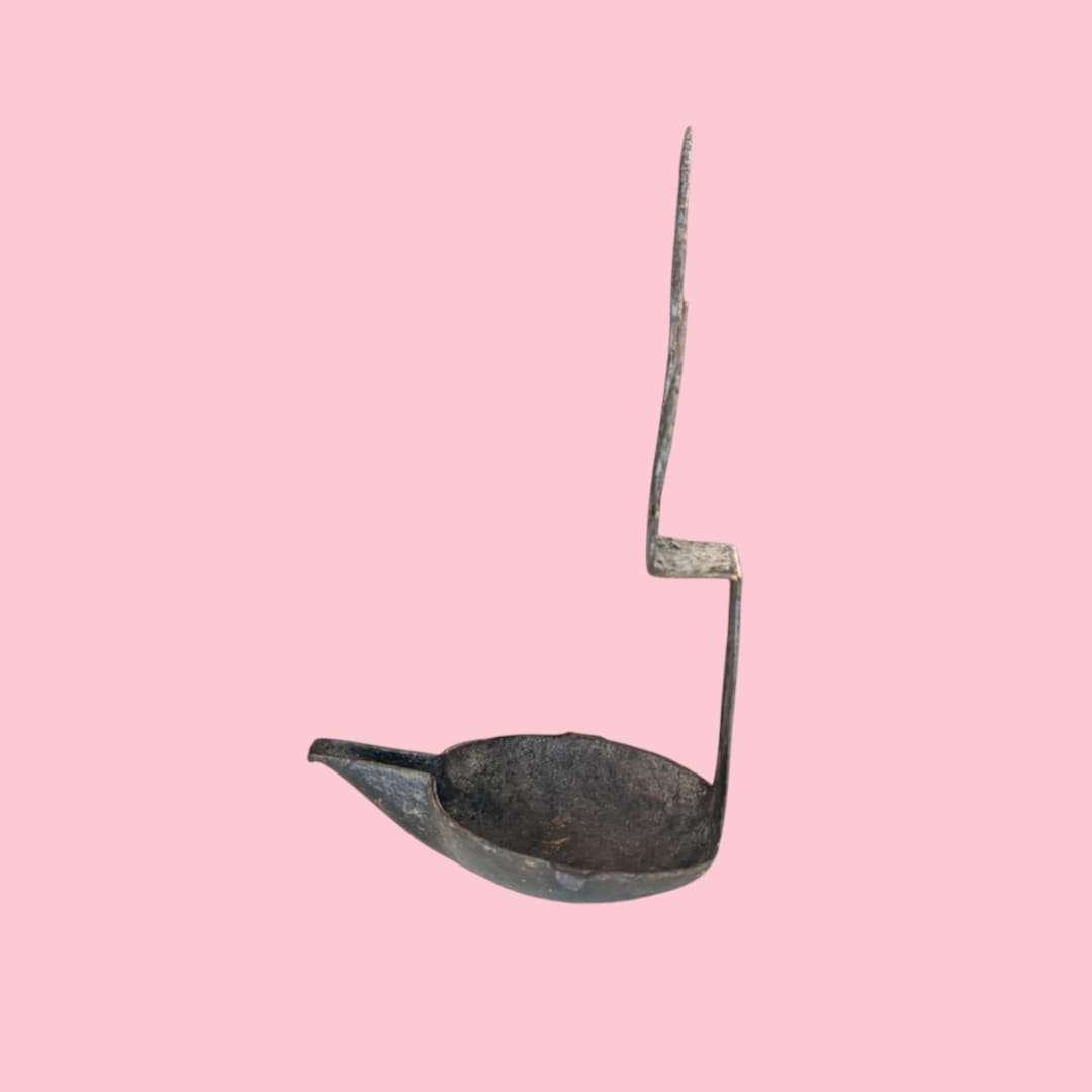 Candil antiguo de hierro forjado sobre fondo rosa claro.