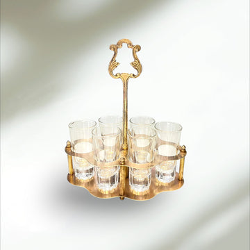 Cañero de metal dorado con seis vasos de cristal vintage, ideal para decoración de hogar o bar con estilo retro elegante.