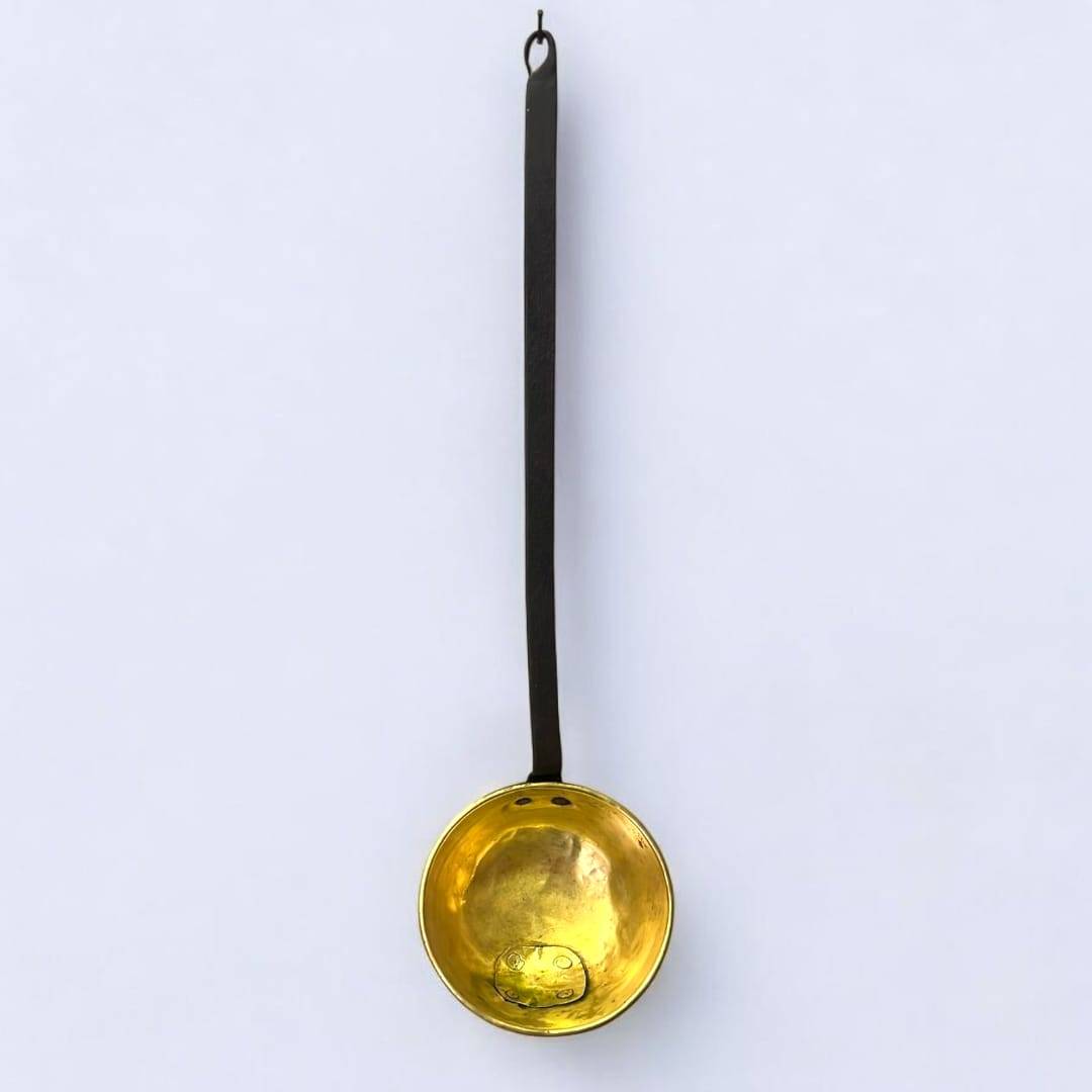 Gran cazo antiguo de metal dorado y hierro forjado con mango largo, ideal para decoración rústica en cocinas o paredes vintage.