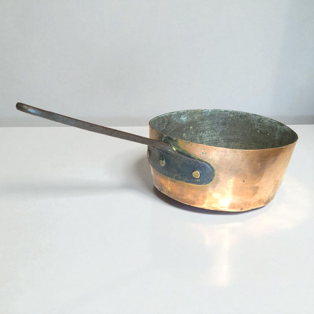 Cazo de cobre con mango de hierro forjado sobre fondo blanco.