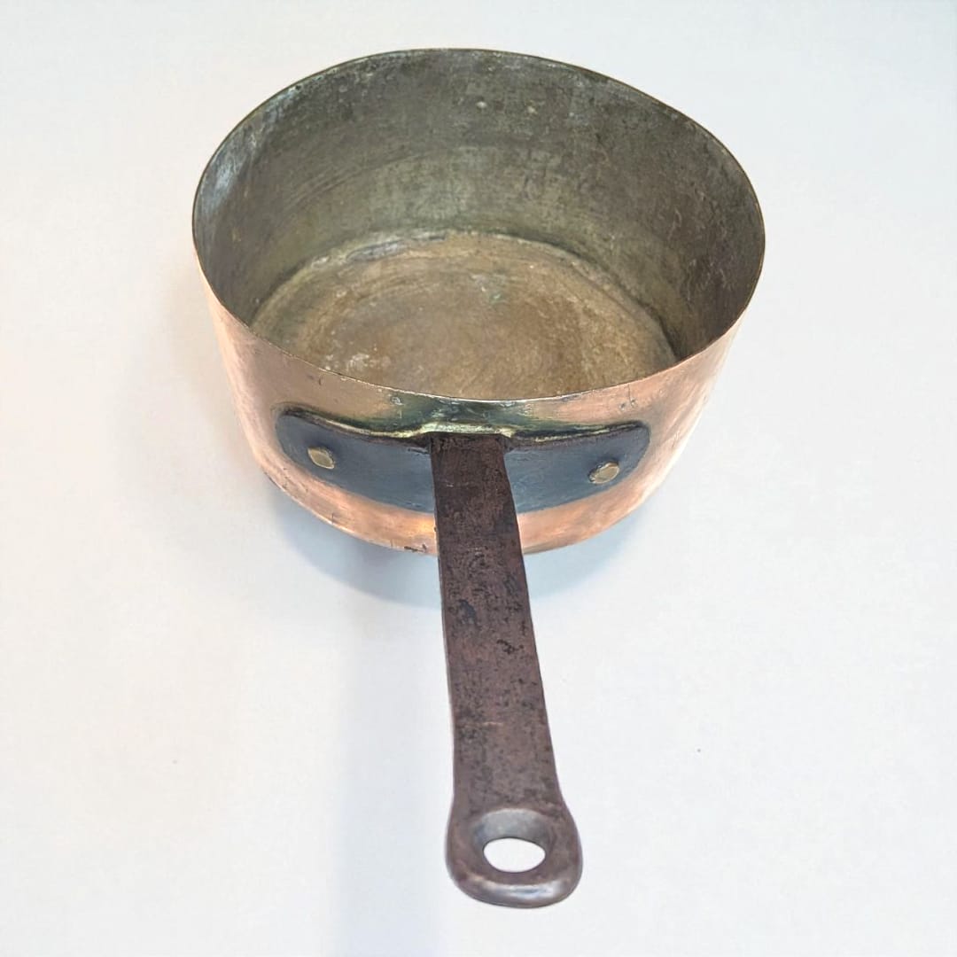 Cazo de cobre con mango de hierro forjado sobre fondo blanco.