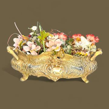 Este Centro de mesa floral de bronce destaca por su cuidada ejecución artística y su marcada inspiración Art Nouveau, visible en cada uno de sus relieves curvos y motivos vegetales.