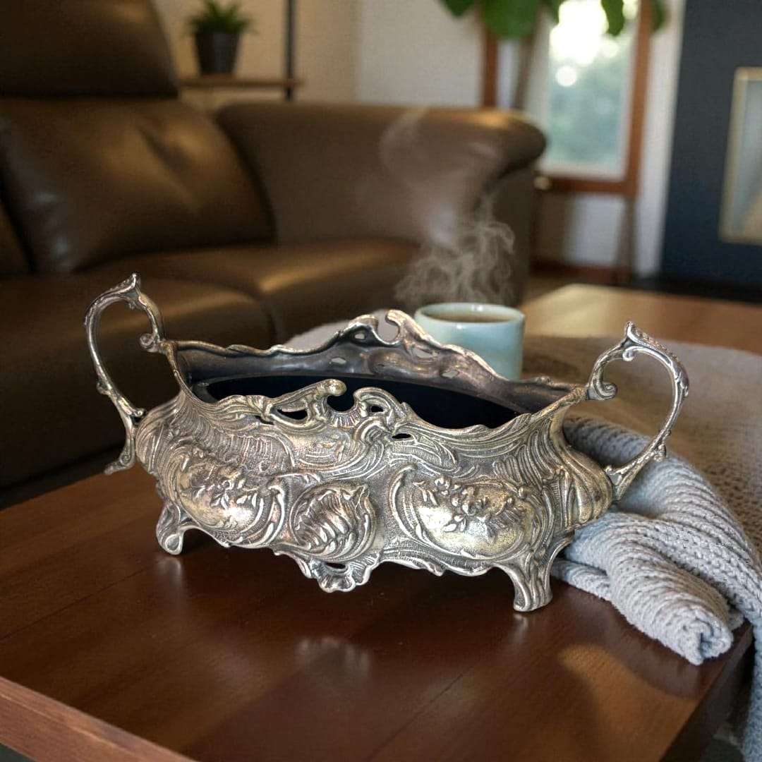 Centro floral de metal plateado con diseño ornamental y asas.