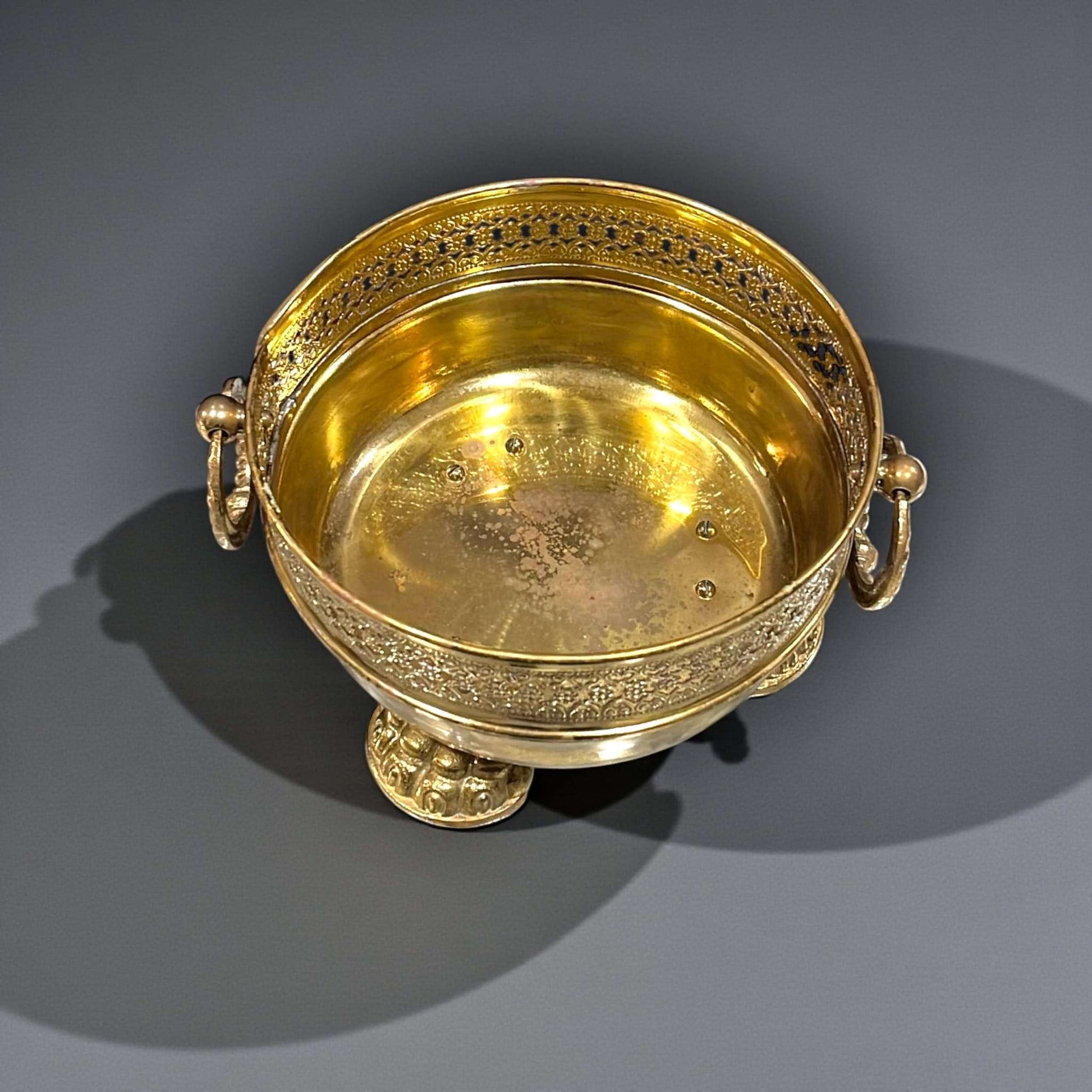 Su estructura sólida se combina con un diseño refinado que destaca por el aro calado, las asas laterales y las patas con forma de garras, elementos que reflejan un trabajo ornamental cuidado y elegante.