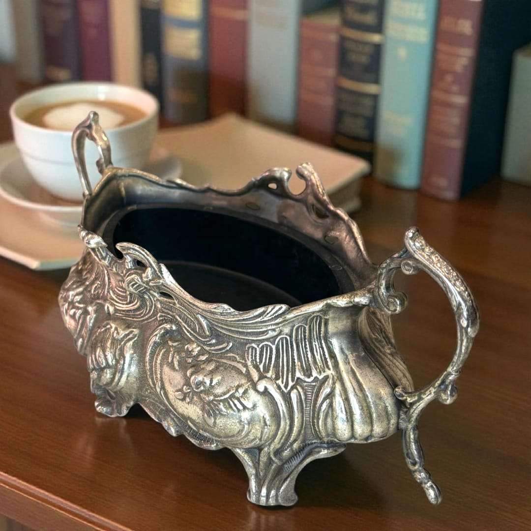 Centro floral plateado con relieves florales y asas curvas.