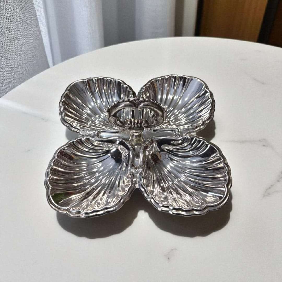 Centro de mesa estilo vintage con cuatro compartimentos en forma de concha y asa decorativa, entremecero de metal plateado para decoración refinada.