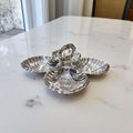 Entremecero antiguo de metal plateado con diseño de conchas y asa central, pieza decorativa funcional para servir en reuniones elegantes.
