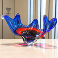 Centro de mesa de cristal Murano rojo y azul con diseño ondulado escultural sobre mesa de mármol.


