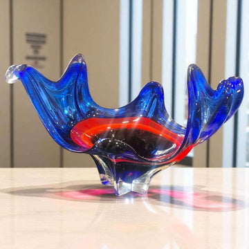Centro de mesa de cristal Murano rojo y azul con diseño ondulado escultural sobre mesa de mármol.

