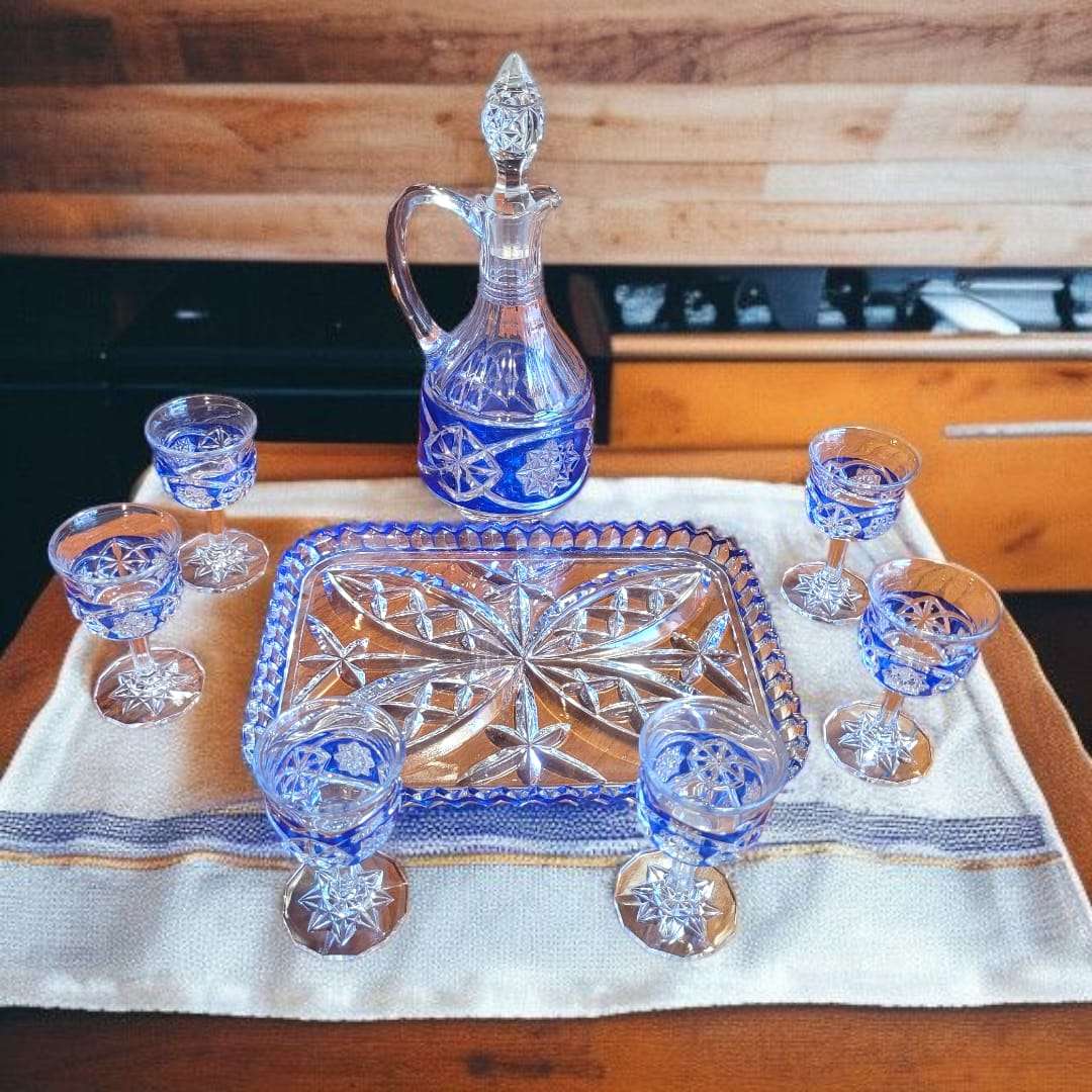 Juego completo de licorera y copas de cristal azul tallado sobre bandeja con diseño geométrico, ideal para decoración de interiores sofisticada.
