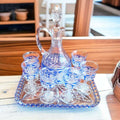 Juego de licorera con copas de cristal azul tallado sobre bandeja decorativa, ideal para decoración elegante en el hogar o jardín.