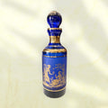 Botella de cristal cobalto con tapón esférico y ribetes dorados.