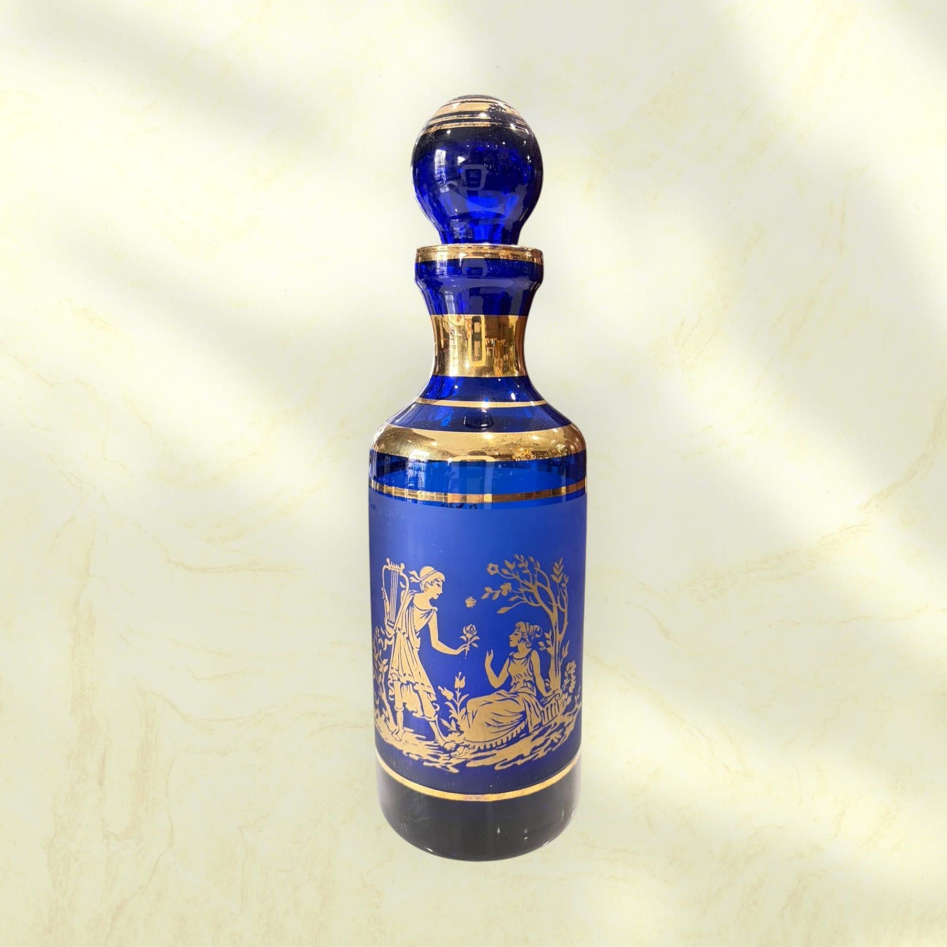 Botella de cristal cobalto con tapón esférico y ribetes dorados.