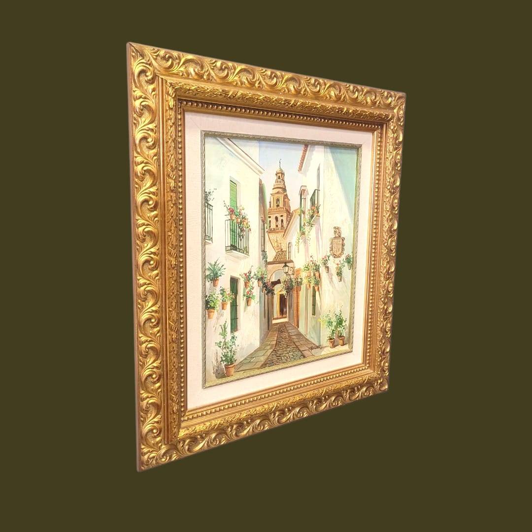Vista lateral del cuadro al óleo Retamero con calle andaluza florida y torre, en marco dorado ornamentado, perfecto para decoración interior.