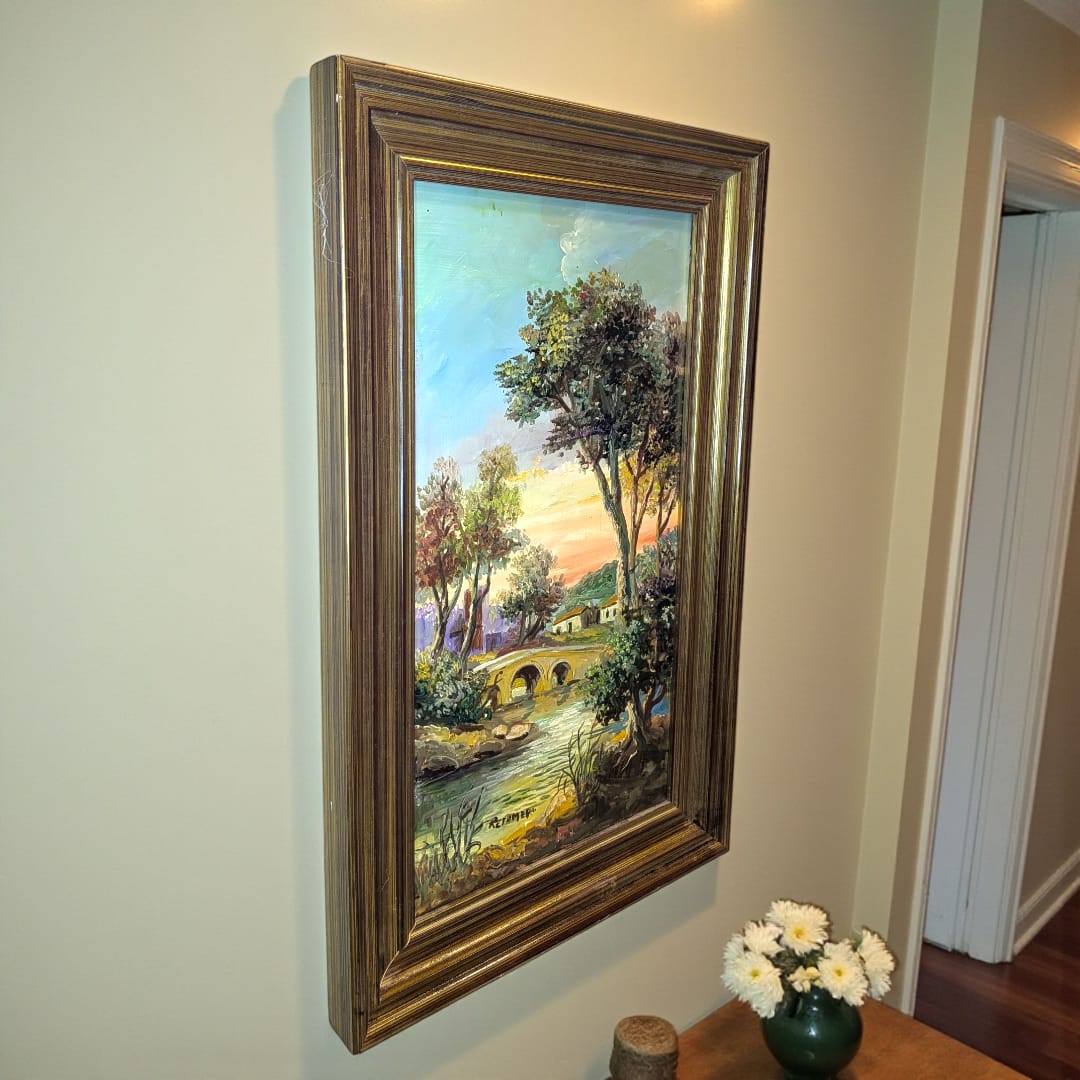 Cuadro de Retamero al óleo, paisaje con puente y río, original enmarcado en dorado, colgado en pared de pasillo interior iluminado.