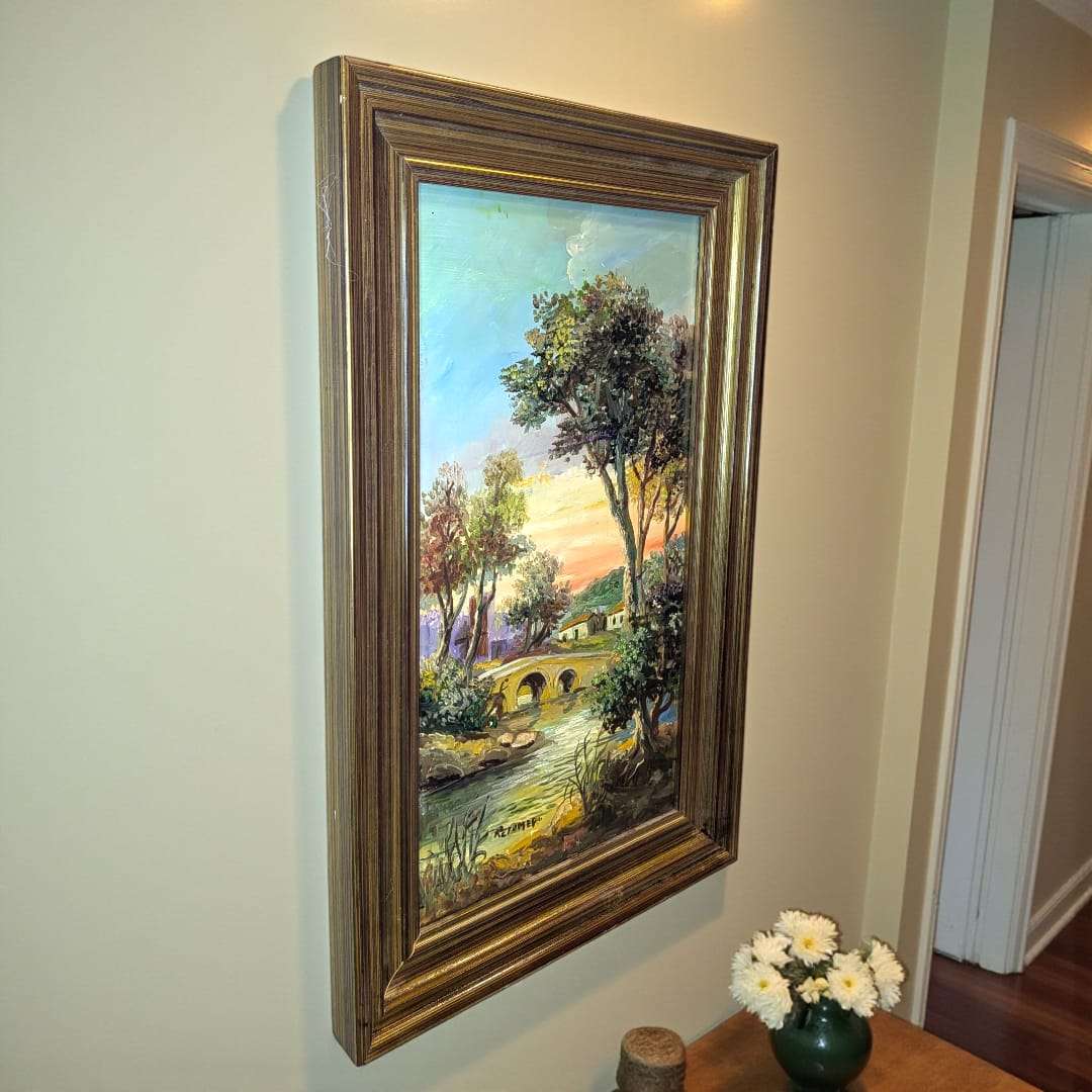 Cuadro de Retamero al óleo, paisaje con puente y río, original enmarcado en dorado, colgado en pared de pasillo interior iluminado.