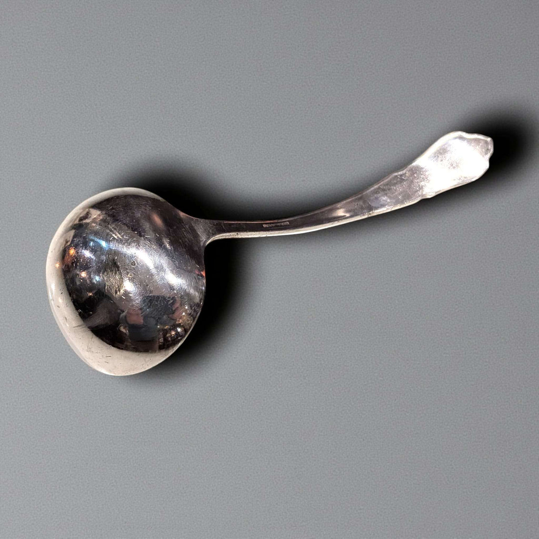 Cucharón de metal plateado antiguo con diseño curvo, ideal para una mesa clásica. Utensilio elegante para servir sopas en decoración vintage.