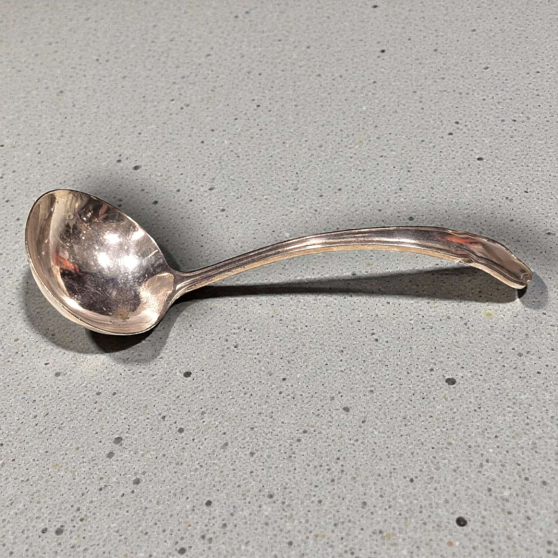 Cucharón de metal plateado antiguo con diseño curvo, ideal para una mesa clásica. Utensilio elegante para servir sopas en decoración vintage.
