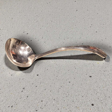 Cucharón de metal plateado antiguo con diseño curvo, ideal para una mesa clásica. Utensilio elegante para servir sopas en decoración vintage.