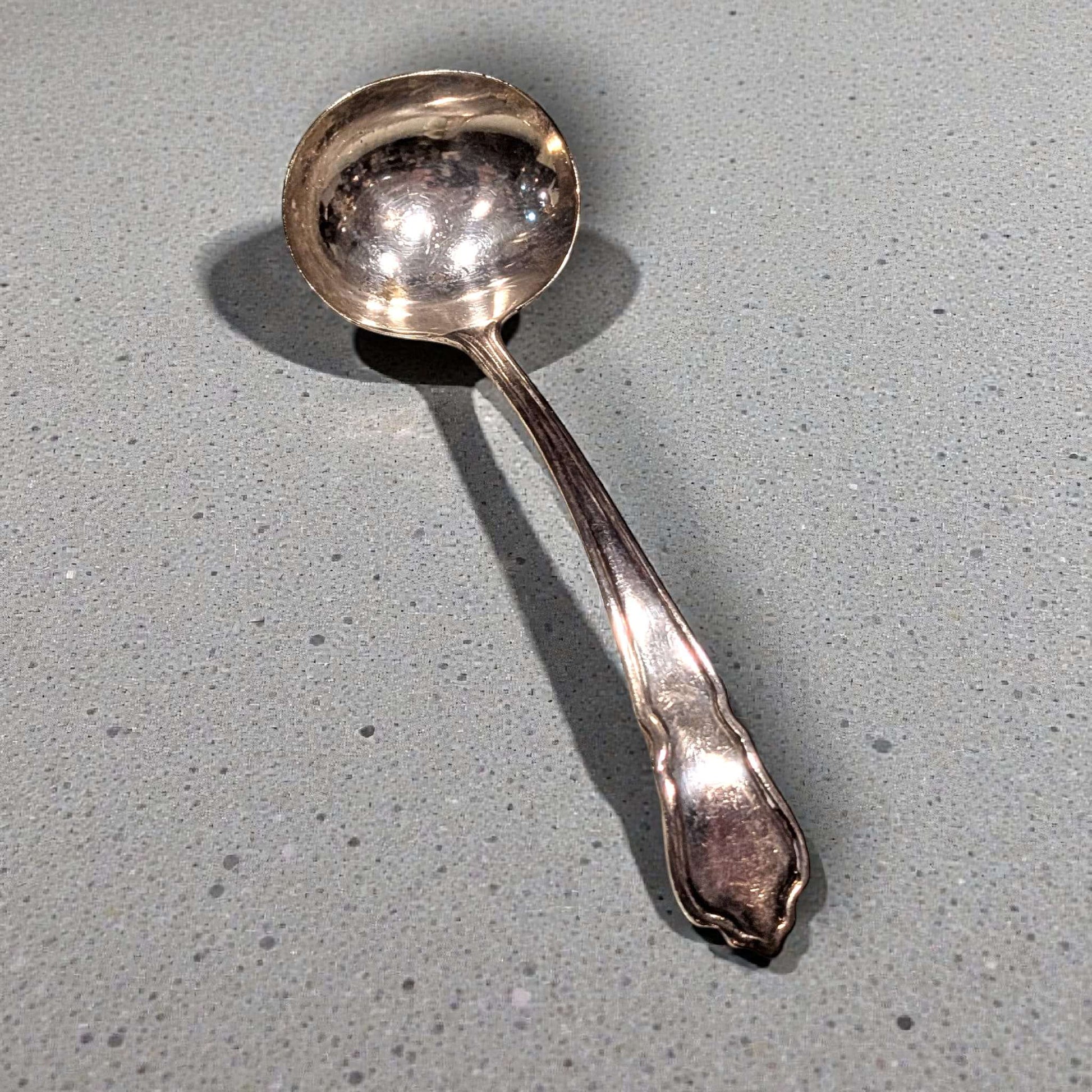 Cucharón de metal plateado antiguo con mango ornamentado, ideal para mesas elegantes. Utensilio decorativo y funcional para servir sopas.