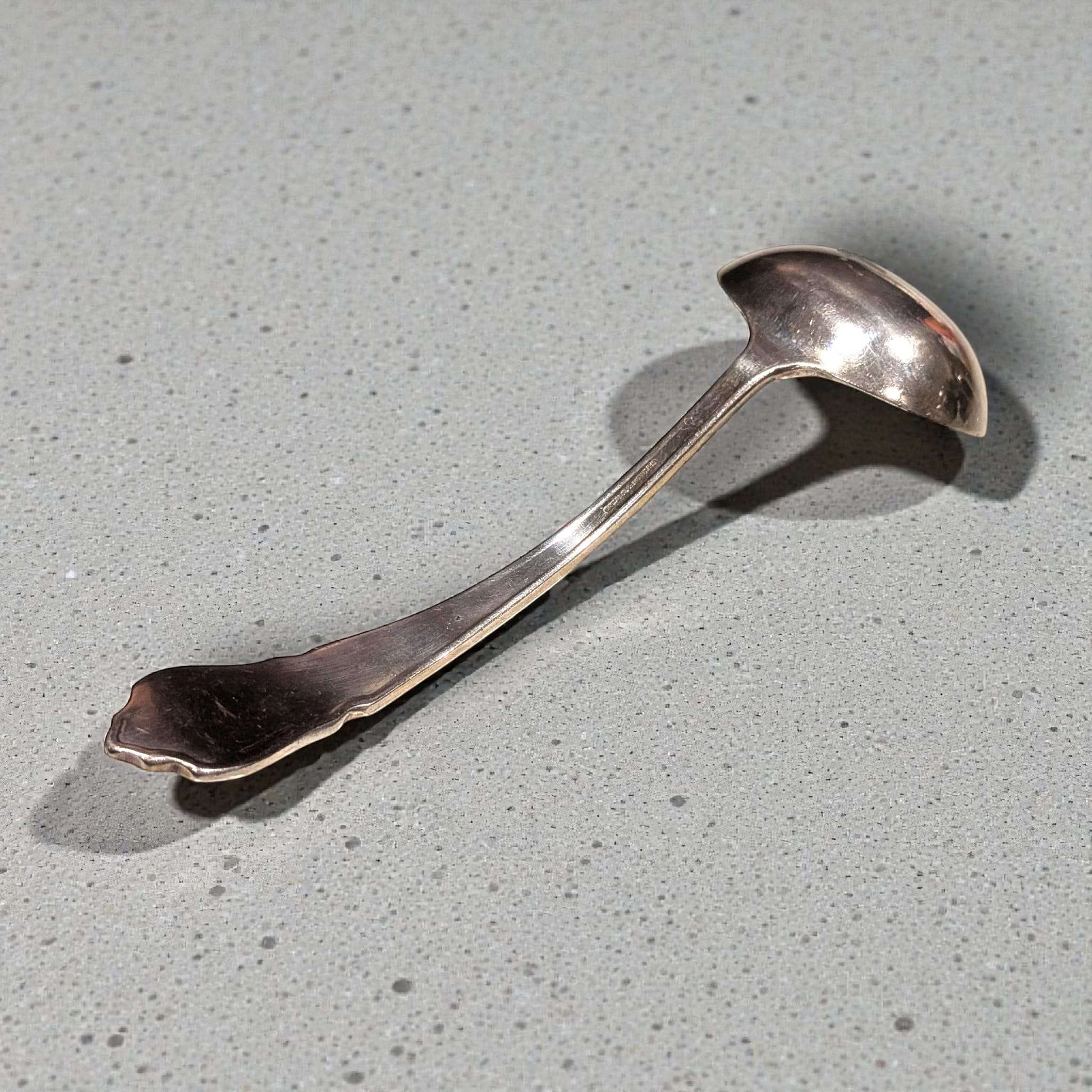 Cucharón clásico de metal plateado con diseño curvo y detalles vintage. Accesorio de cocina ideal para decoración de mesa refinada.