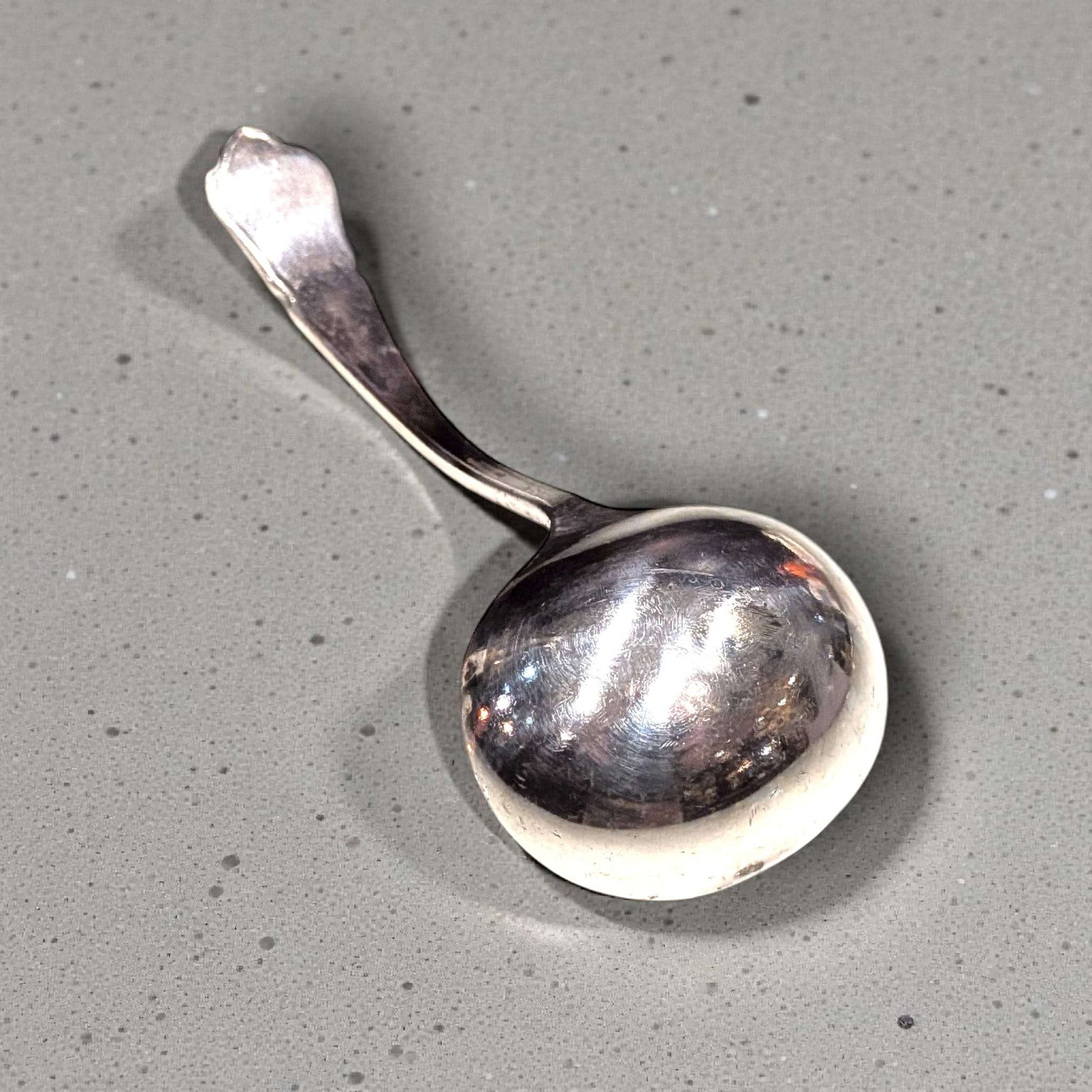 Cucharón de alpaca con forma redondeada y acabado pulido, perfecto para servir caldos. Estilo antiguo para decoración de cocina elegante.