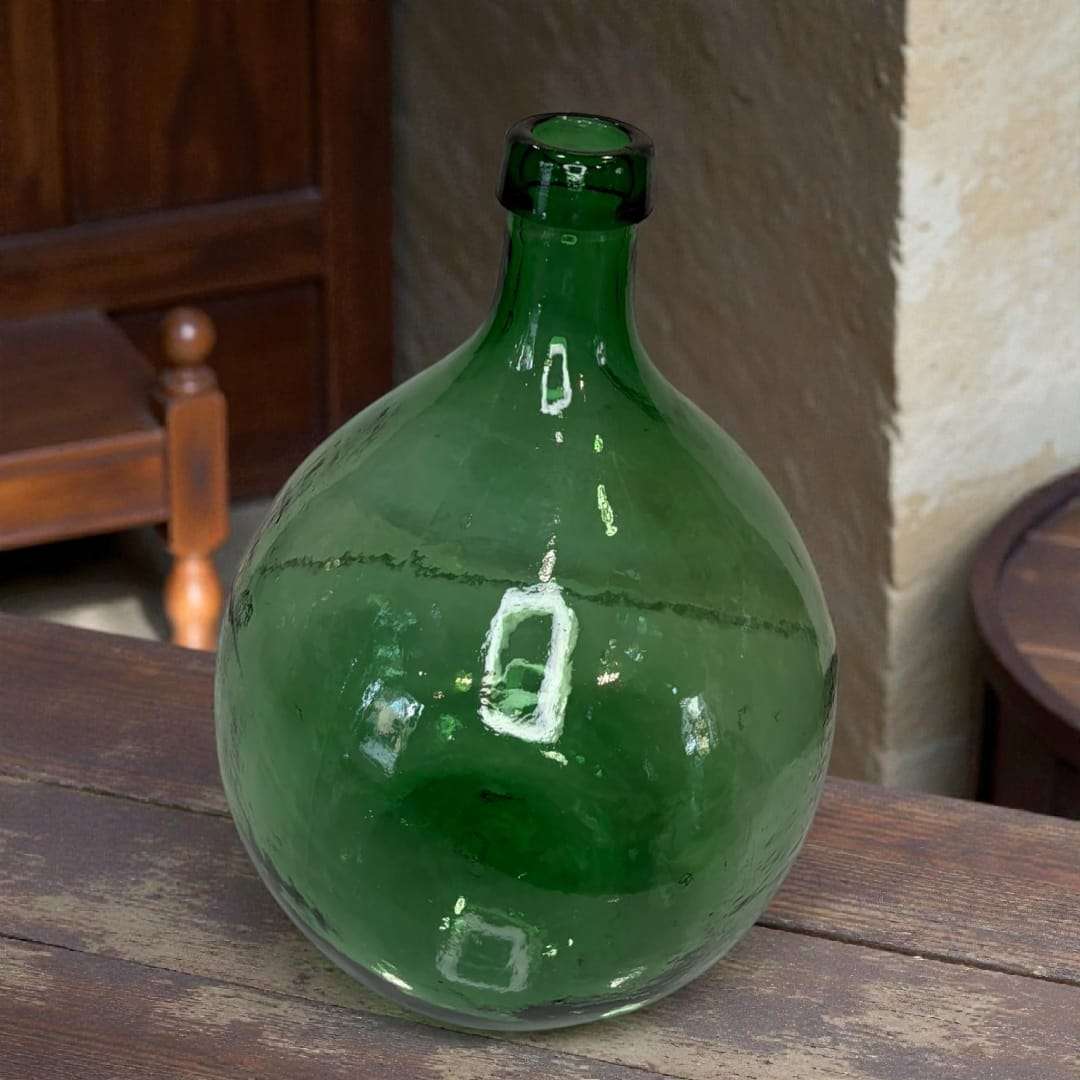 Damajuana antigua de vidrio verde soplado con acabado rústico, ideal para decoración vintage en interiores de estilo clásico o bodegas.