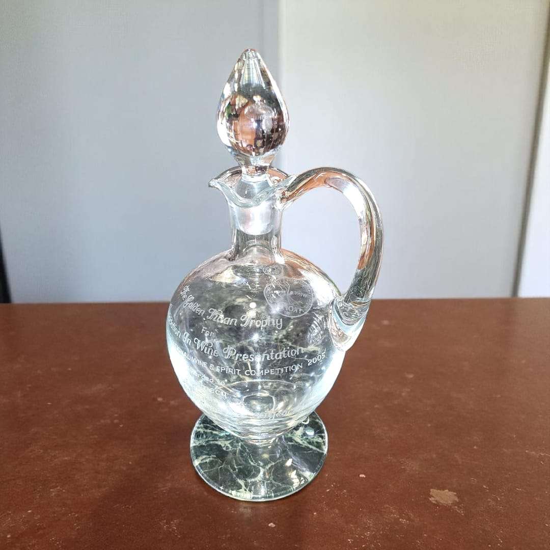 Vista frontal del decantador de cristal con tapa y grabado legible.