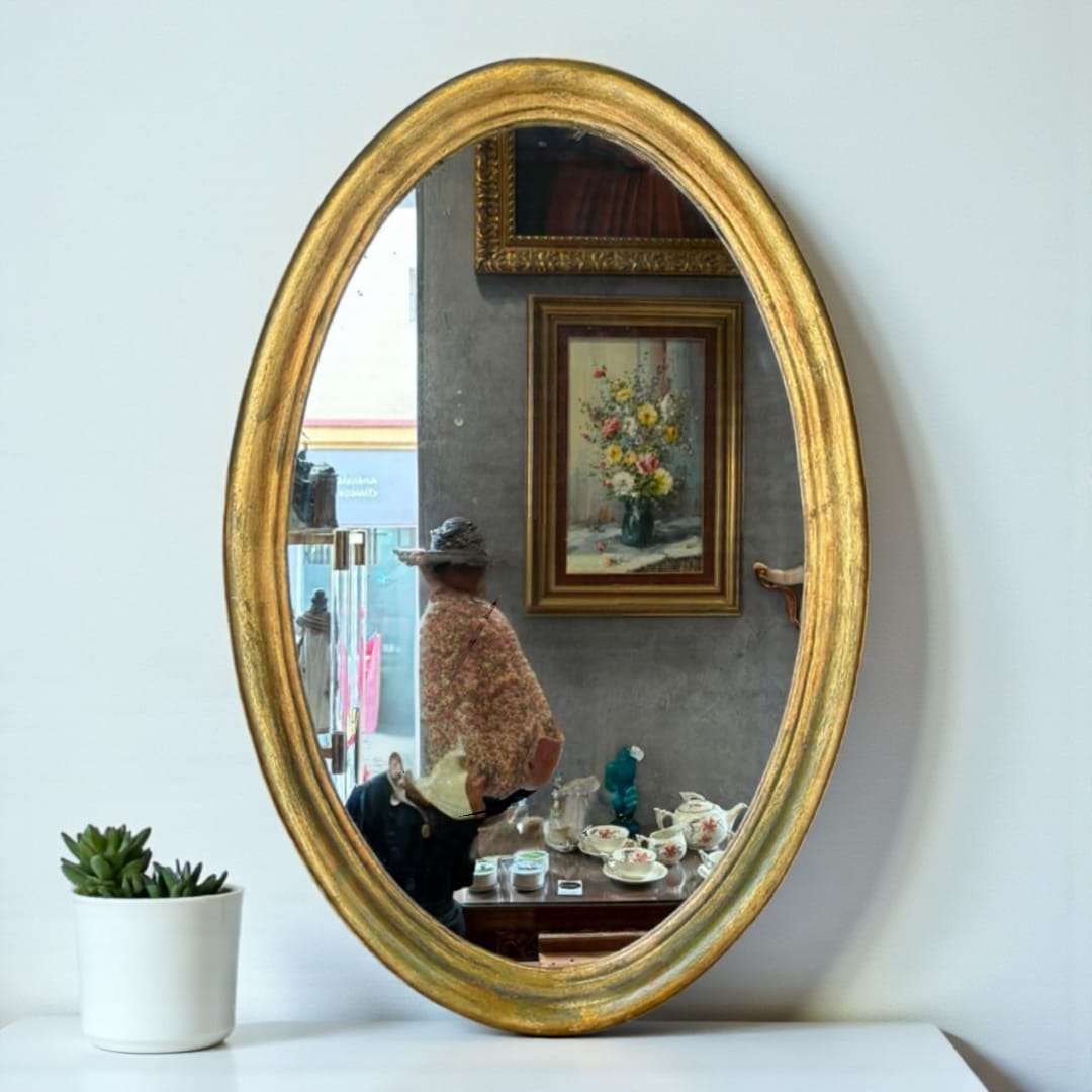 Espejo ovalado dorado colgado sobre pared blanca