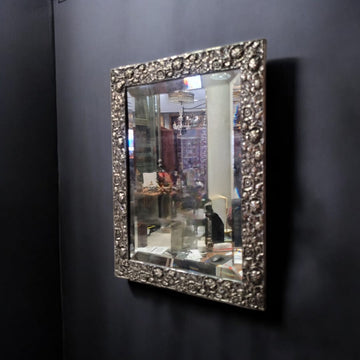 Espejo biselado con marco en metal plateado antiguo colgado en pared oscura. Ideal para decoración clásica en interiores elegantes o vintage.