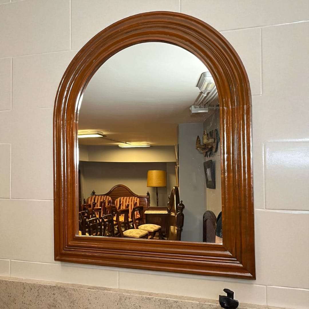 Vista lateral del espejo de caoba semi ovalado en ambiente clásico.