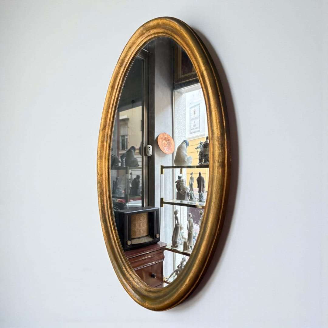 Espejo ovalado dorado colgado sobre pared blanca