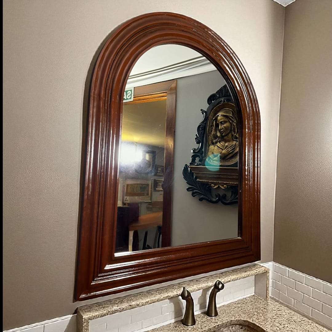 Espejo antiguo de caoba semi ovalado colgado en pared.