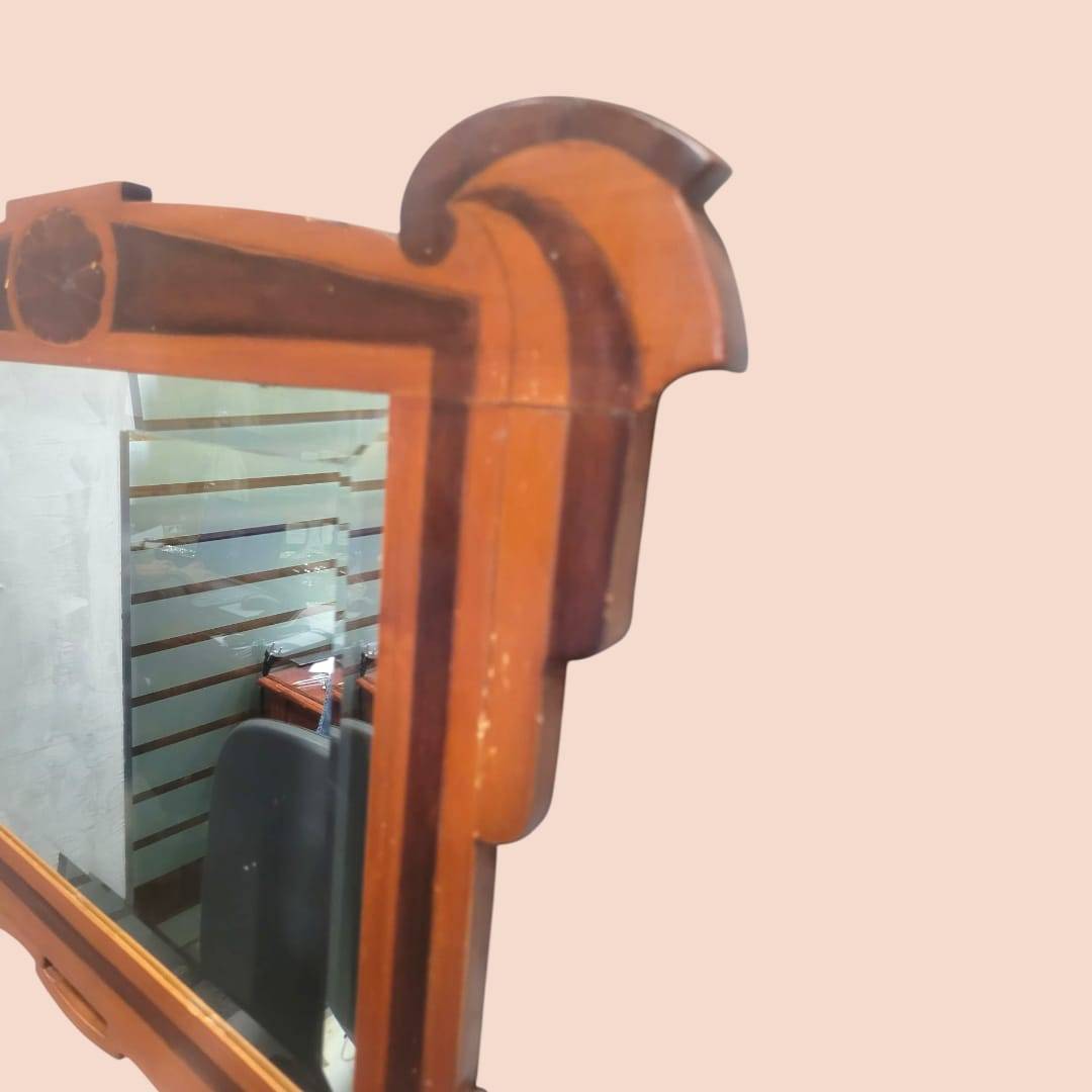 Detalle del marco superior del espejo de madera con cristal biselado, acabado clásico y elegante para decoración de hogar estilo retro o antiguo.